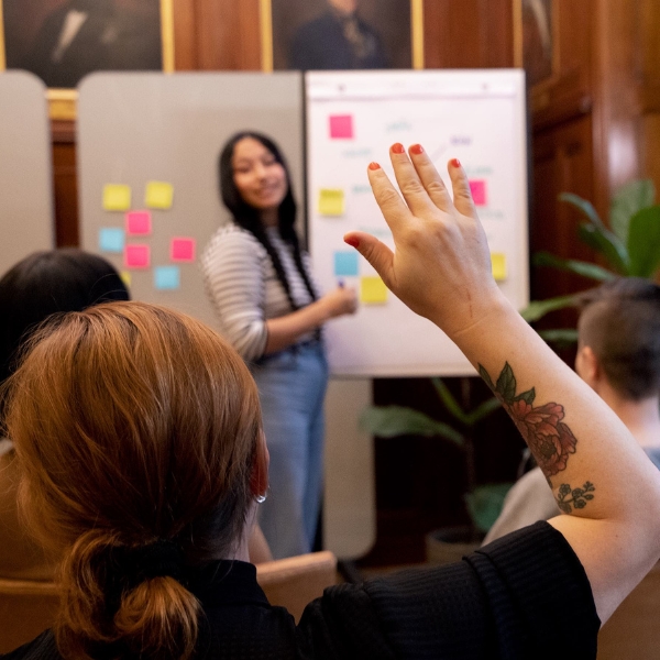 Utbildare från RFSL Utbildning står framför en whiteboard. Person i publiken räcker upp en hand.